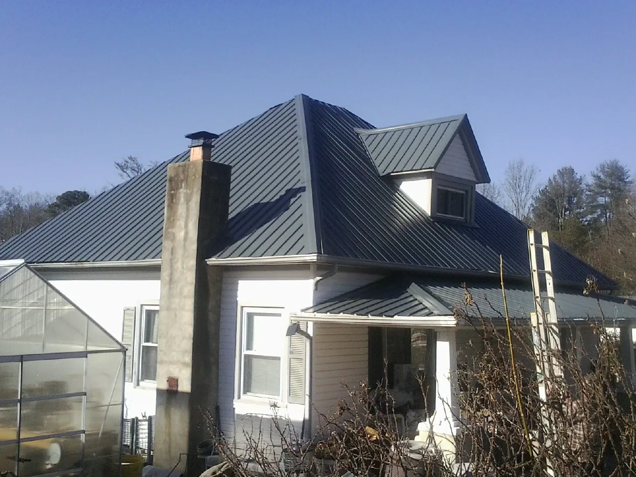 Dark blue standing seam metal roof on a white farmhouse with dormer — Slate & Tile Roof Repair by Roofing Brothers in Crystal Springs
