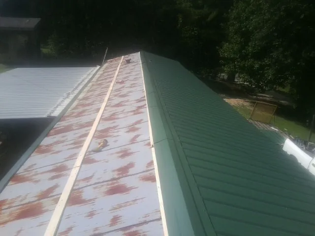 Old rusted panels beside newly installed green metal roofing — Wind Damage Roof Repair by Roofing Brothers in Crystal Springs