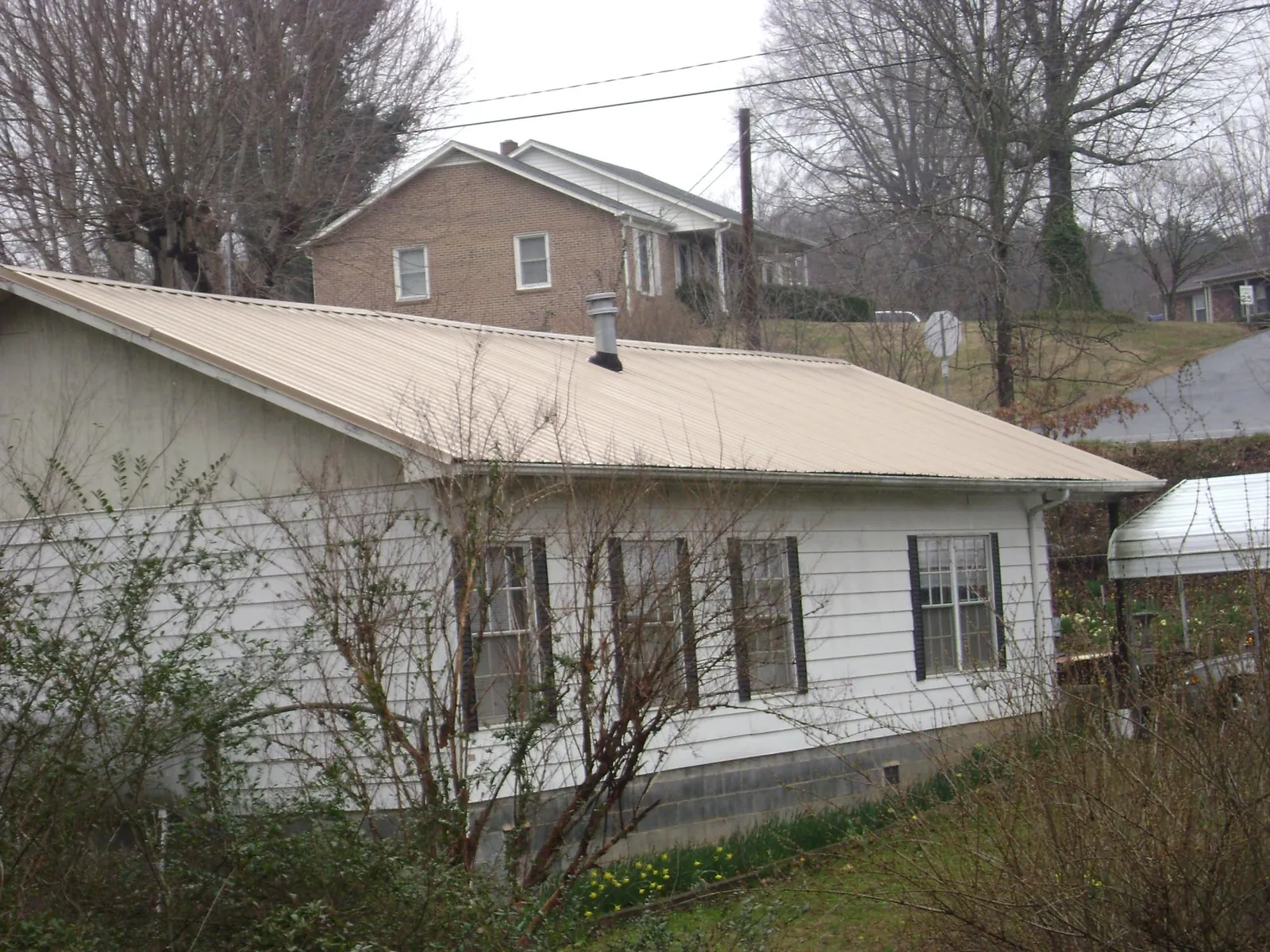 Tan metal roof on a white sided house set into a hillside — Commercial Roofing by Roofing Brothers in Crystal Springs